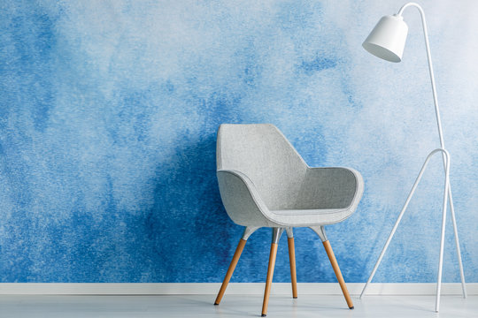 Chair and white lamp set on an empty, blue wall. Place your product