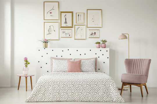 Feminine bedroom interior with a double bed with dotted sheets, armchair, art collection and plants