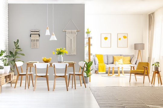 White chairs at wooden dining table in bright apartment interior with yellow armchair. Real photo