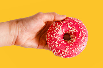 Hand holding a pink donut on orange background.