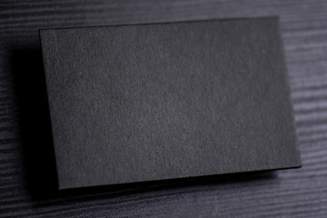 Mockup of blank textured black business card on dark wood background