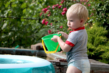 A little boy is playing with water near an inflatable pool. Summer and family holidays. Happy childhood