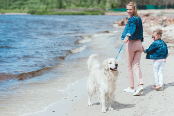 happy mother and daughter walking with golden retriever dog on sea shore