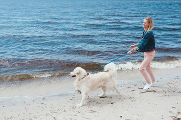 attractive happy woman walking with dog on sea shore