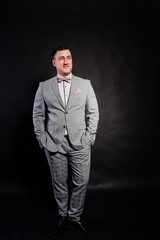 Studio portrait of man in gray suit and bow tie against black background.