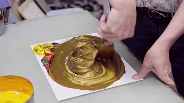 man mixes paint until golden in color, to print logo on packaging products