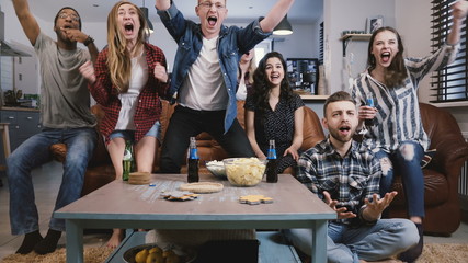 Friends watch sports on TV, celebrate success. Crazy football supporters fans group shout with arms...
