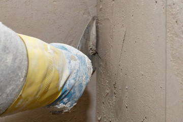 Hand with a spatula in the process of leveling the raw plaster.
