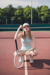 Portrait of young Caucasian teen model wearing fashionable tennis dress, posing on tennis hardcourt, summer sunny day outdoors. Fashion portrait shoot