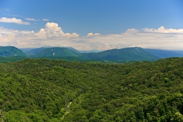 Naklejka na ściany i meble Panorama of a large valley between mountains covered with forest. Sunny day. Beautiful cumulus clouds over the tops of mountains against a blue sky.