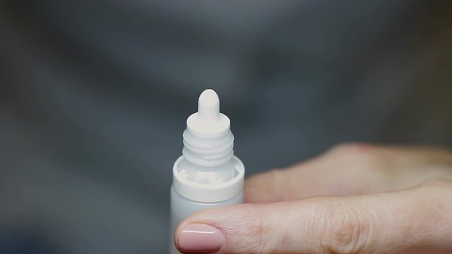 Woman twists off white cap of spray, uses it and closes the plastic bottle