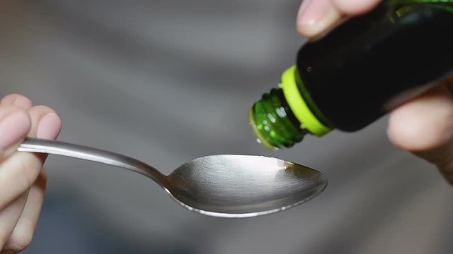 Woman drops six drops of brown liquid mixture on tablespoon out of green bottle