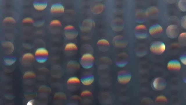 Abstract bokeh holiday background in slow motion. Decoration of playing colored light. Christmas and new year iridescent lights on dark background. Rainbow of defocused crystal bead hangings in HD.