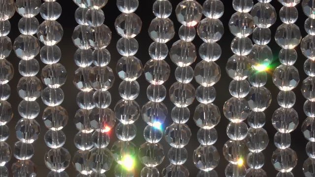 Crystal bead hangings, sparkling with multicolor specks on dark background. Holiday background with amazing texture in slow motion. High speed camera shooting.
