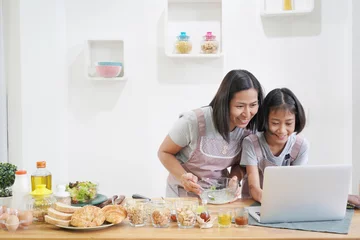 Photo sur Aluminium Cuisinier Mère et fille apprennent à cuisiner à l& 39 aide d& 39 un ordinateur portable dans la cuisine à la maison, concept asiatique de famille heureuse