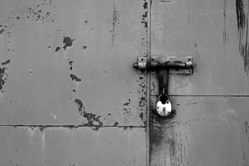 Old padlock on metal gate in black and white.