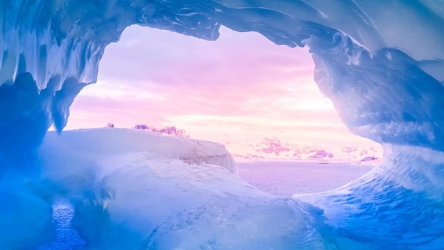 Blue ice cave in Antarctica covered with snow and flooded with soft sunset pink light. Exploring beauty world. Travel background. Slow motion 4K footage
