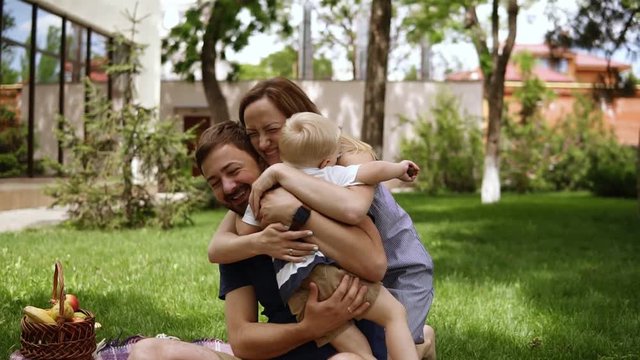 Happy family of three. Parents in casual are sitting on a plaid with opened hands and smiling to their little son. Child is running to them. Hugging, smiling
