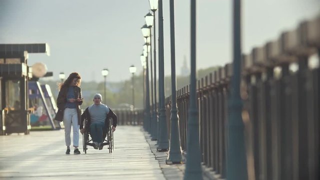 Disabled man in a wheelchair walking together her girlfriend on the quay