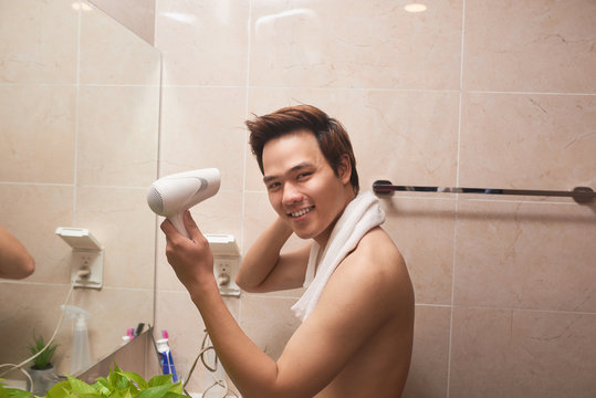 Young Asian Man Blow Drying Hair In Bathroom