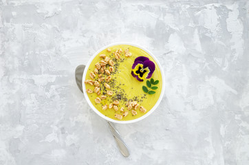 Yellow smoothie bowl with Chia seeds, air wheat and pansy flower on concrete background