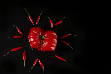 pomidor otoczony przez ostre papryczki na czarnym tle