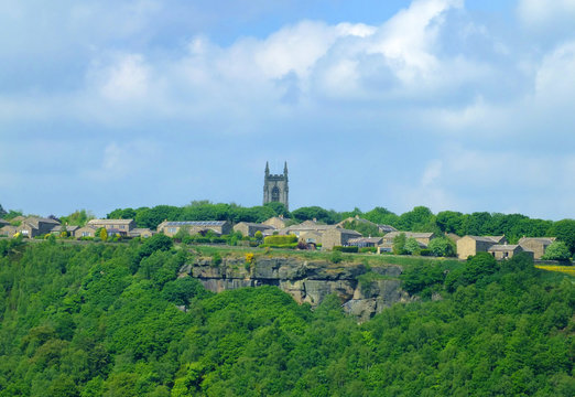 the pennine village of heptonstall viewed from across the calder valley with historic church houses and surrounding woodland and steep rocky hills