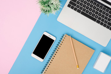 Office desk working space - Flat lay top view mockup photo of working space with laptop, mock up smartphone and blank notebook on pastel background. Blue pink color background working desk concept.