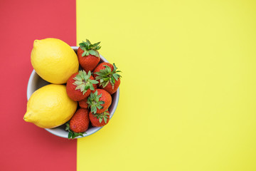 Fresh lemons and strawberries in a bowl on a yellow and red background. Flat lay, top view
