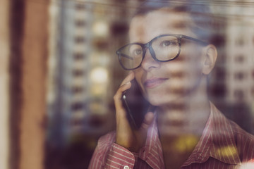 Attractive young woman talking on the phone, view through the office window. A business female uses a smartphone.