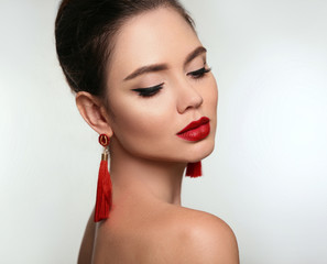 Beautiful girl with earrings jewelry. Beauty face of young brunette woman with a bright make-up and red lips isolated on studio background. Fashion, make-up, cosmetics, hairstyle.