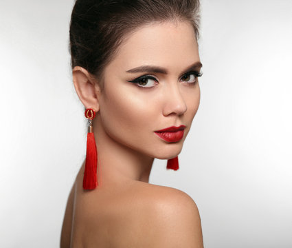 Beautiful girl with earrings jewelry. Beauty face of young brunette woman with a bright make-up and red lips isolated on studio background. Fashion, make-up, cosmetics, hairstyle.