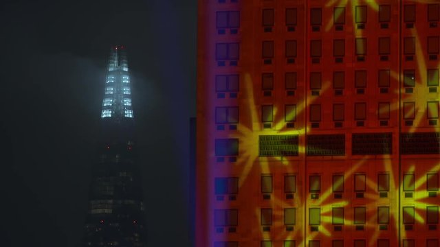 A long shot of two buildings in London during a light show, including projecting onto buildings.