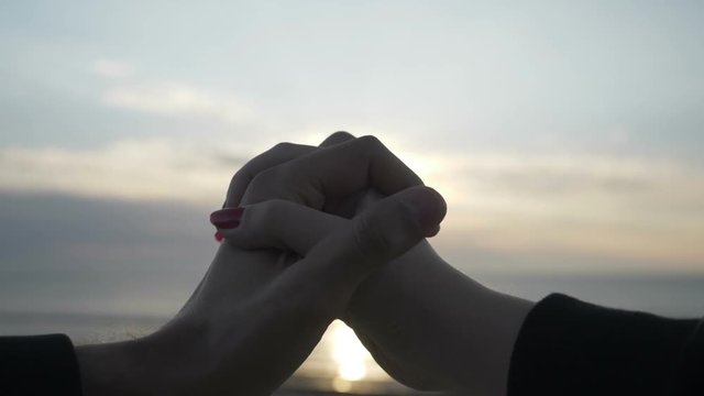 Silhouette of holding hands making heart shape with sunset inside on the beach in slow motion