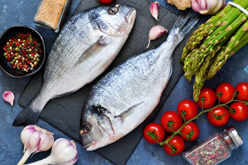 Fresh, raw Dorado fish with asparagus, tomatoes and spices on a concrete background. Ingredients for cooking.