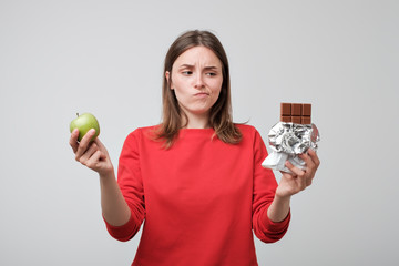 Woman holding a green apple and a chocolate. Concept of healthy diet