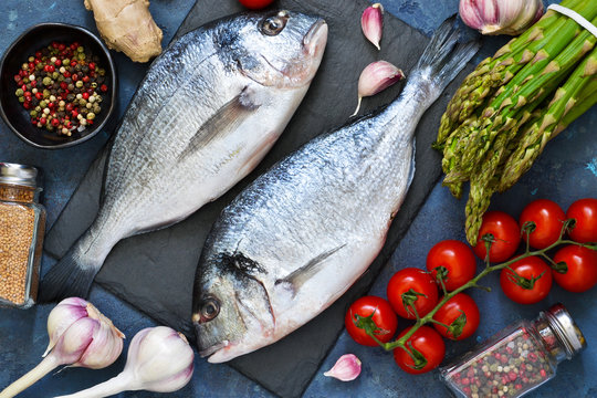 Fresh, raw Dorado fish with asparagus, tomatoes and spices on a concrete background. Ingredients for cooking.