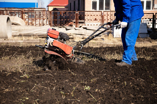 Worker With A Machine Cultivator Digs The Soil In The Garden