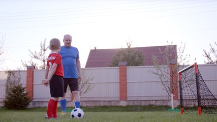 Granfather is playing football with his grandson on the lawn at the backyard
