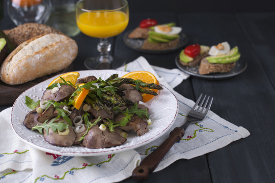 A delicious healthy dinner, a warm chicken liver salad with oranges and rucola, on a black wooden background. Orange juice and fresh bread with avocado. Free space for text. Copy space
