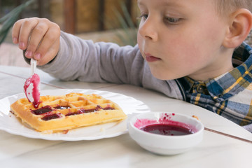 A little boy eats dessert (Belgian waffles with jam) in a cafe.