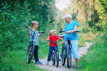 Obraz premium happy grandmother with kids riding bikes in nature