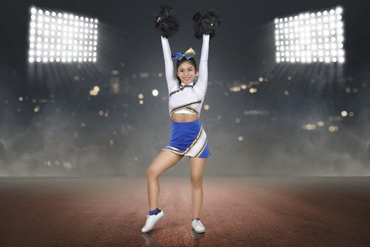 Pretty asian cheerleader with hands holding pom-poms in the air