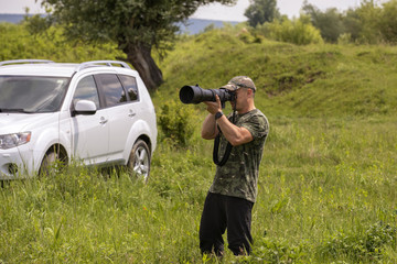 A bird watcher and bird photographer with a large telephoto lens, in a field