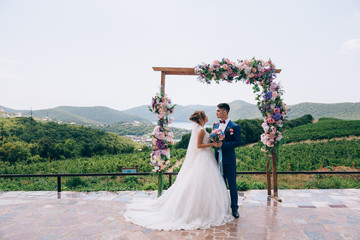 Newlyweds in love look at each other and enjoy the wedding day. They stand on an arch of pink,...