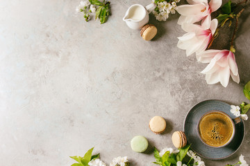Fototapeta na wymiar Blue cup of black espresso coffee french dessert macaroons, cream and spring flowers magnolia, blooming cherry branches over grey texture background. Top view, space. Spring greeting card, wallpapers