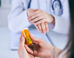 Female medicine doctor hand hold jar of pills and explain how to take pills to patient at...
