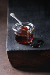 Homemade liquid transparent brown sugar caramel in glass jar standing on black wooden board with spoon.