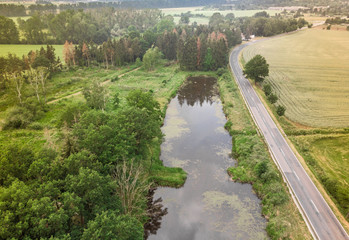 Fototapeta na wymiar Aerial view of a small pond parallel to a country road in Saxony-Anhalt with fields and forests in the surrounding area