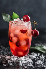 Fresh cherry cocktail. Fresh summer cocktail with cherry and ice cubes. Glass of cherry soda drink on dark stone background.